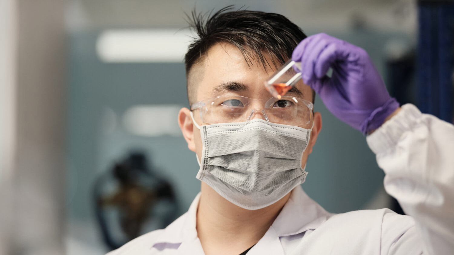 asian male lab tech viewing test tube contents